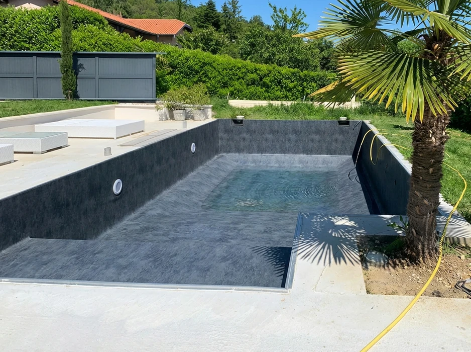 Piscine rectangulaire en cours de remplissage, liner PVC armé anthracite texturé, projecteurs LED encastrés en inox, escalier intégré à marches larges, niche de volet roulant immergé
