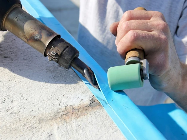 Technicien en combinaison bleue effectuant l'entretien d'une piscine extérieure rectangulaire à eau turquoise, utilisant une épuisette télescopique pour nettoyer la surface